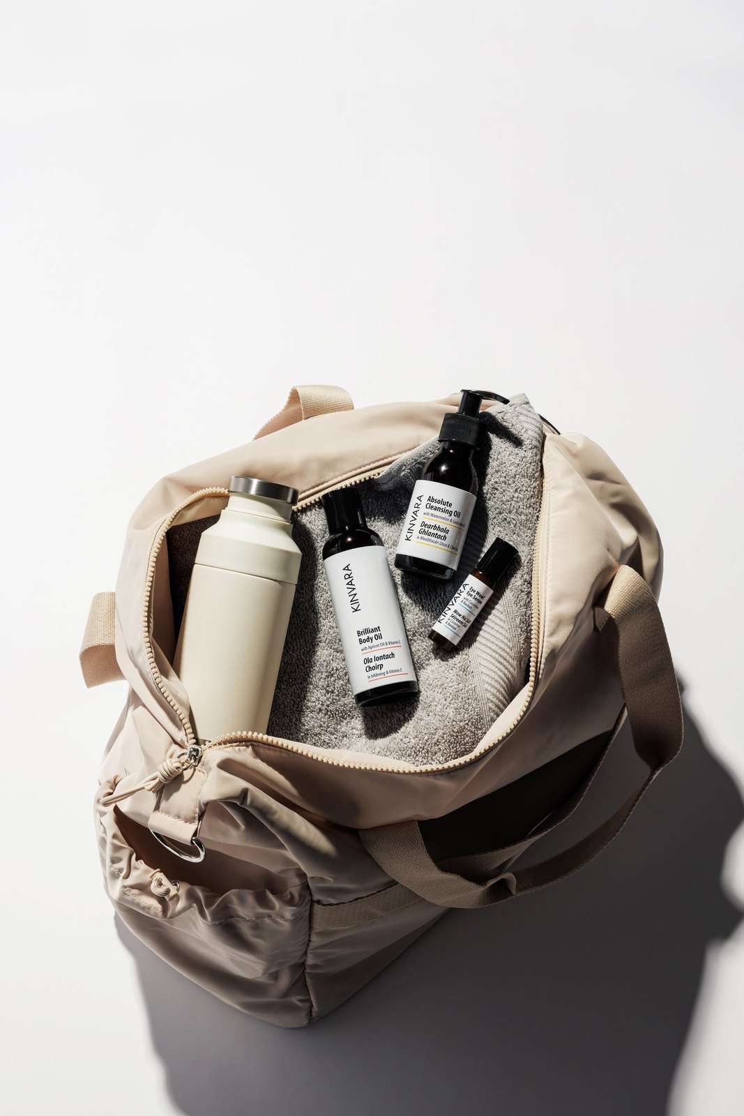 Kinvara bottles and a rolled towel packed inside an open canvas weekender bag