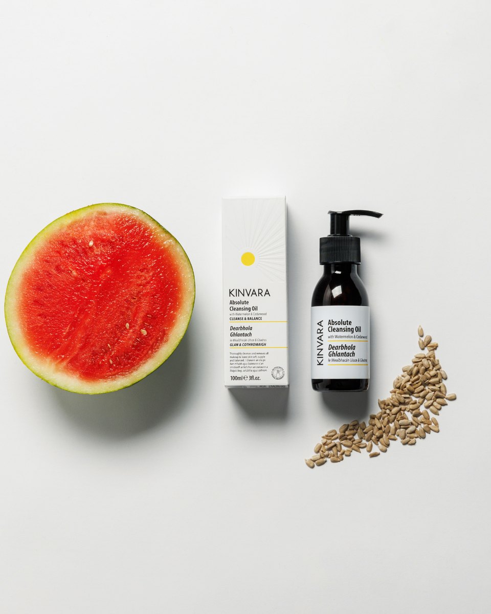 The cleansing oil carton and bottle beside a halved watermelon and dried seed heads